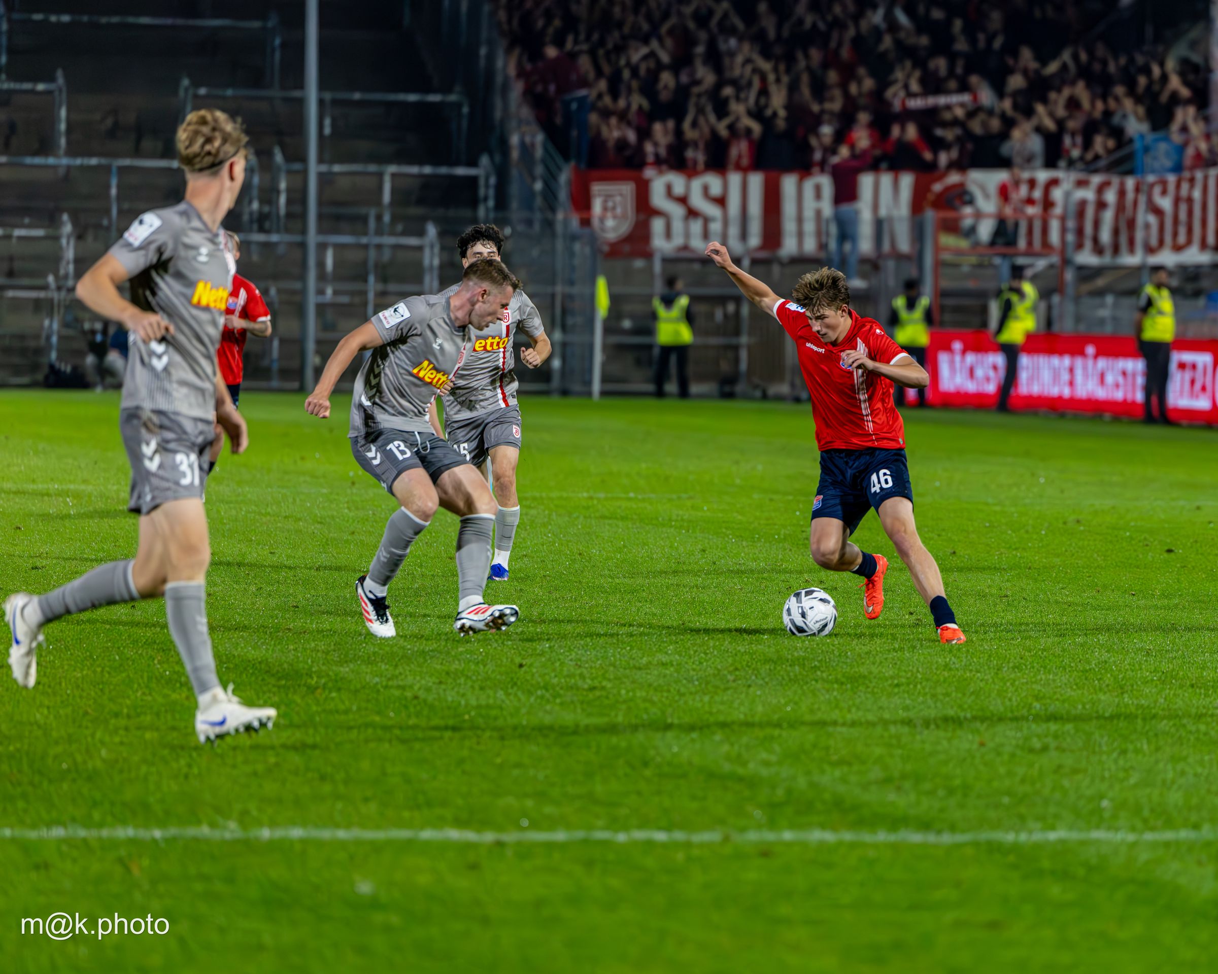 SpVgg Unterhaching player dribbling past opponents in front of a full stand